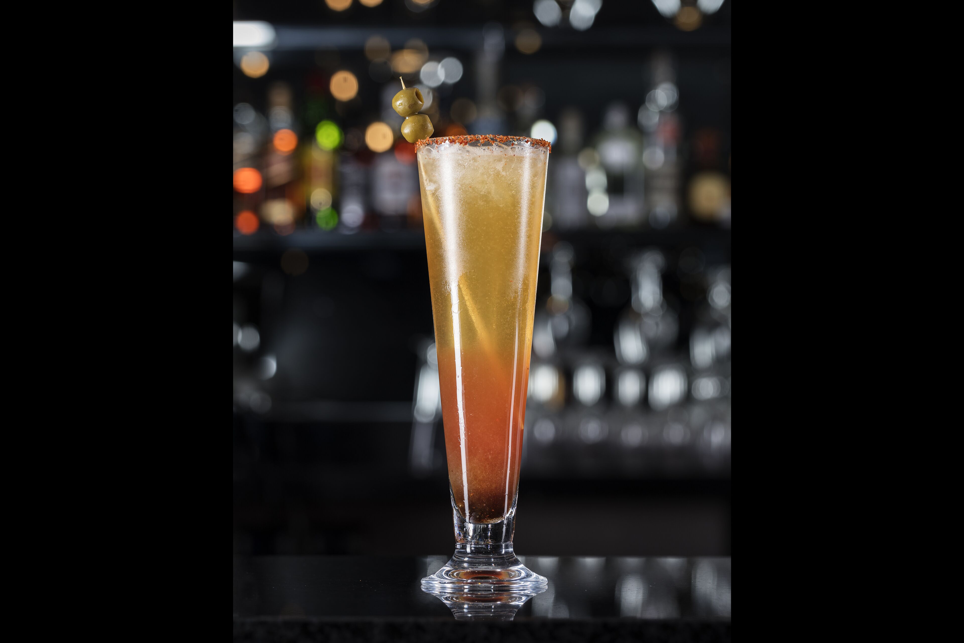Un bicchiere alto con sfumature di colore, probabilmente contenente un cocktail, e guarnito.