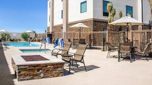 Zona de piscina con sillones de descanso, sombrillas y una chimenea de piedra.