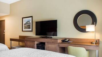 A hotel room with a bed, a desk with a flat-screen TV, a microwave, a telephone, and a mirror.