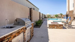 Una cocina exterior con pileta y parrilla, un área de piscina con sillones de descanso y un patio con pisos de piedra.