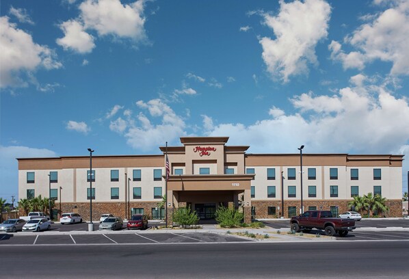 Um hotel Hampton Inn com um estacionamento e vários carros estacionados na frente.