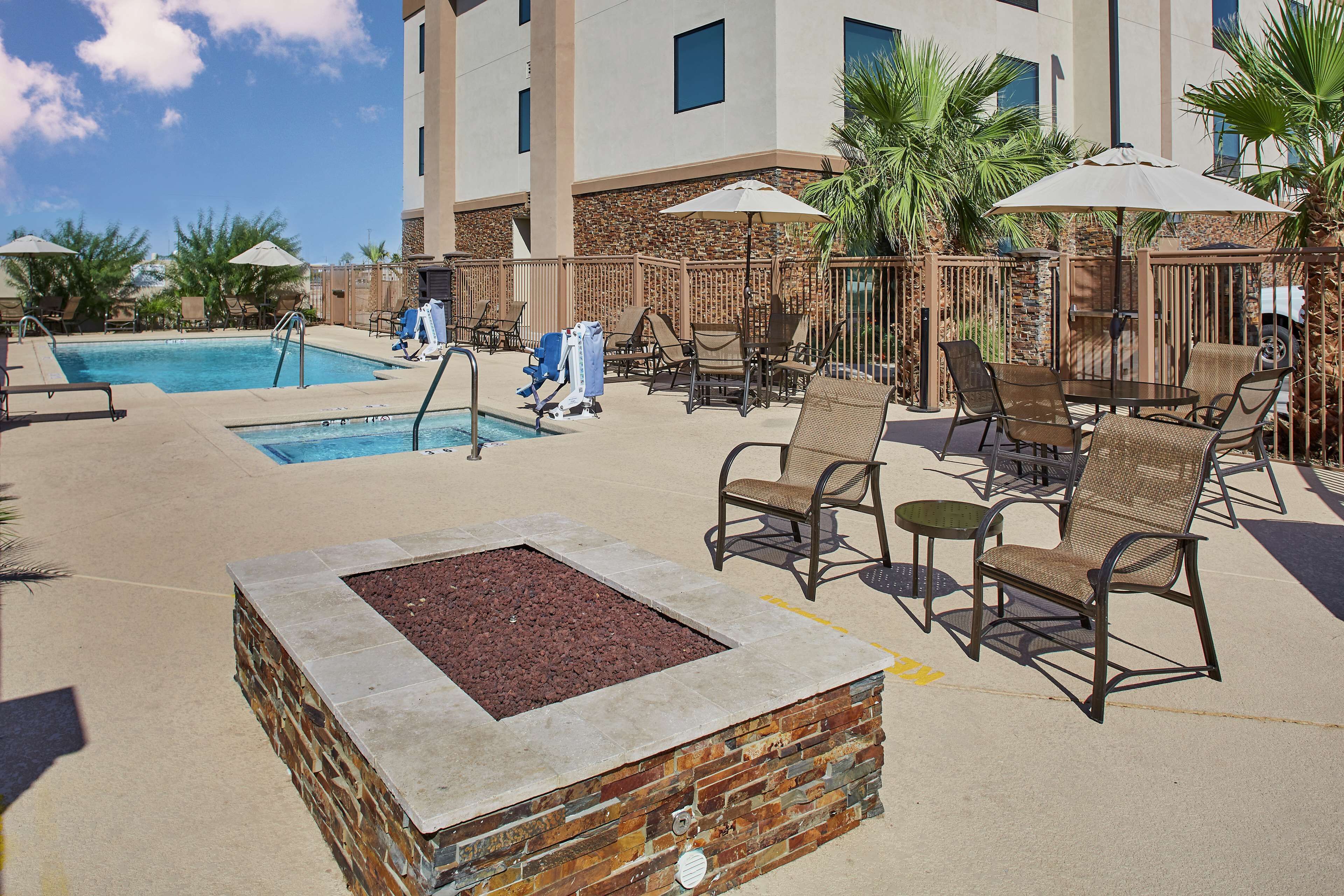 A poolside area with lounge chairs, umbrellas, and a small fire pit.