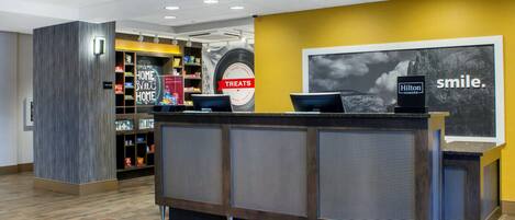 A hotel reception desk with a 'Hilton Honors' sign, a 'Treats' sign, and a 'Home Sweet Home' sign.