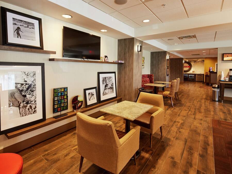 A hotel lobby with framed photographs on the walls, a flat-screen TV, and a seating area with tables and chairs.