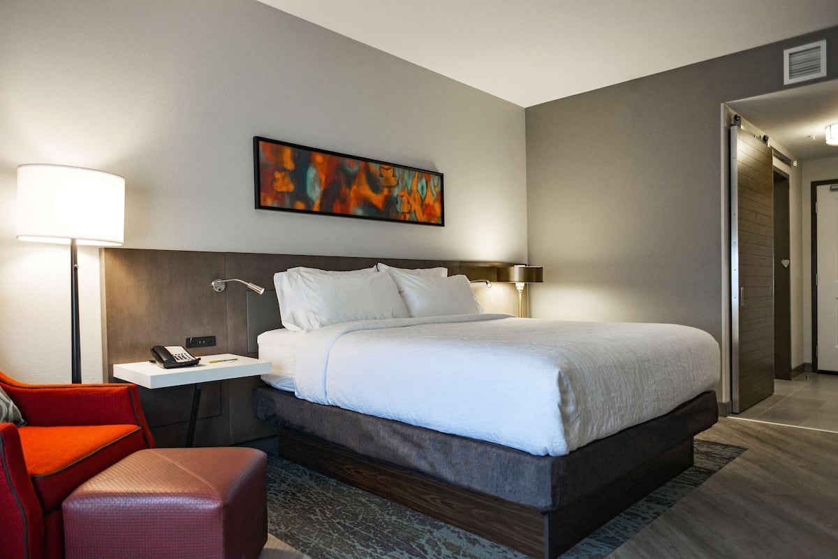 A hotel room with a bed, a desk, a chair, and a painting on the wall.