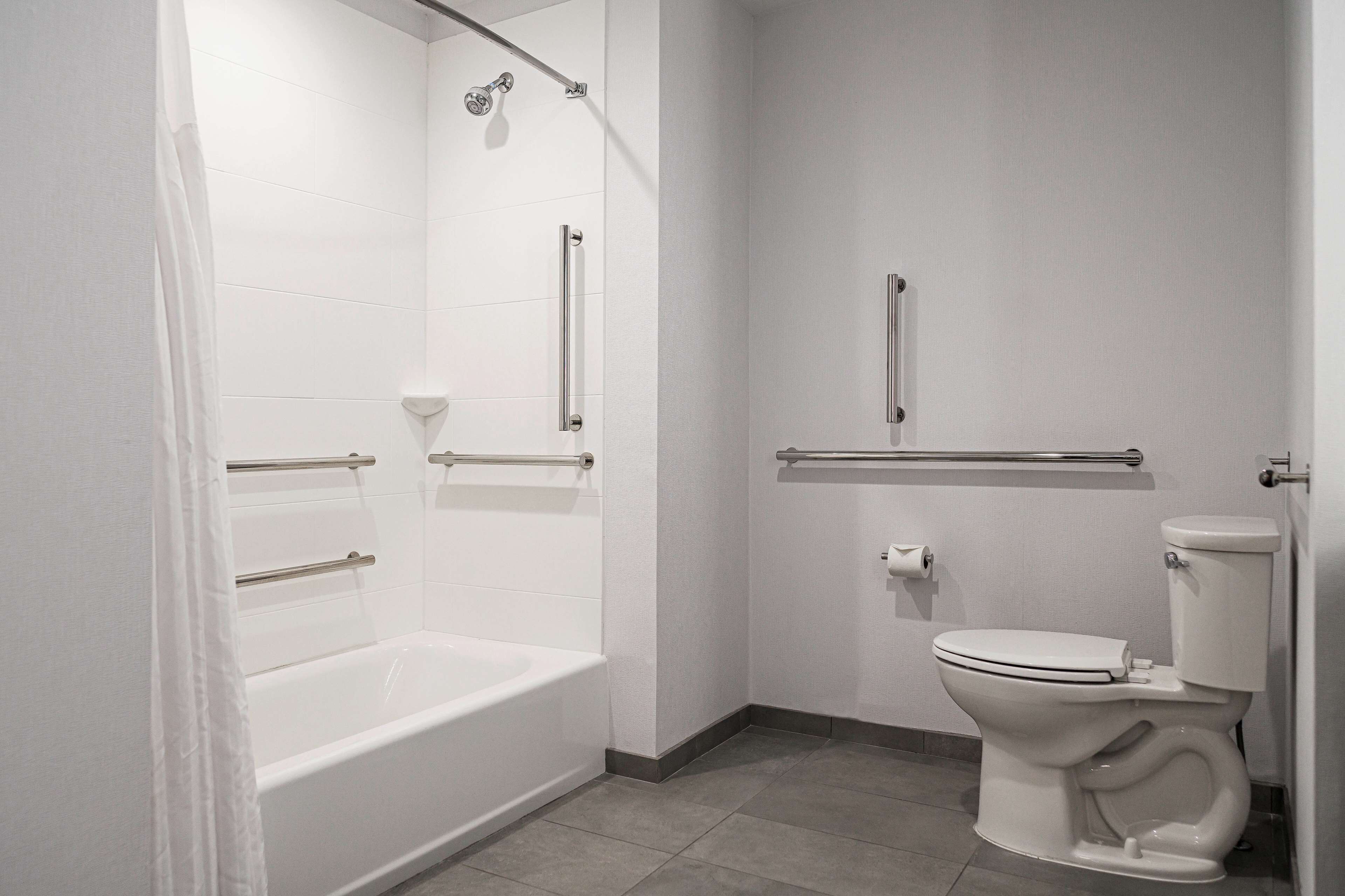 Un baño moderno con bañera, inodoro y barras de apoyo.