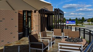 A hotel patio with outdoor seating, a fire pit, and a view of the Hilton Garden Inn sign. - Hilton Garden Inn Louisville Mall of St. Matthews (Louisville)