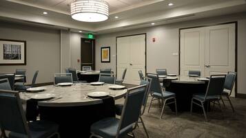 A conference room with a large oval table, multiple chairs, a door with an exit sign, and a framed picture on the wall.