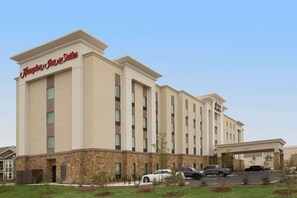 Un hotel Hampton Inn & Suites con fachada de piedra, varios espacios de estacionamiento y cielo despejado.