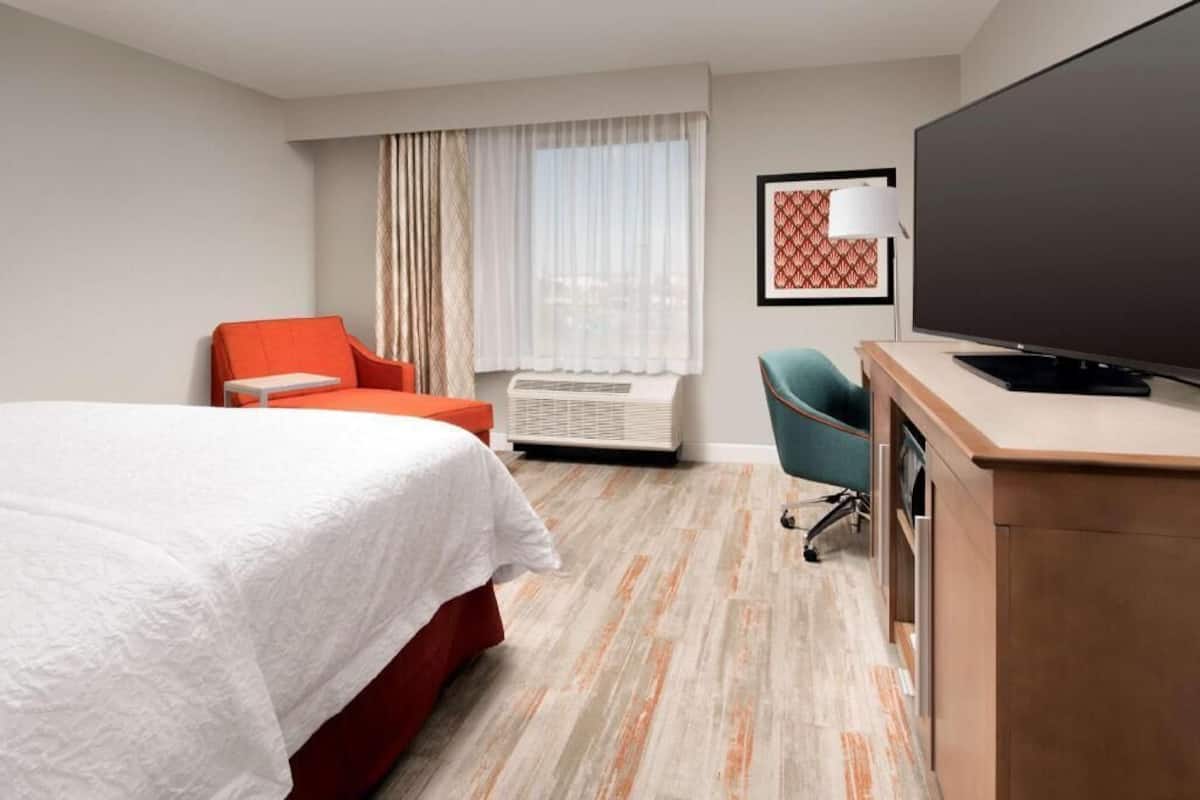 Una habitación de hotel con cama, escritorio, televisor, silla y aire acondicionado.