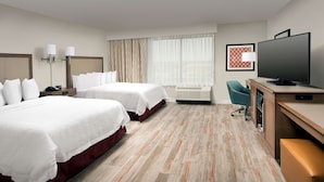 A hotel room with two beds, a desk with a television, a chair, and a large window with curtains. - Hampton Inn & Suites San Antonio Lackland AFB SeaWorld (San Antonio)