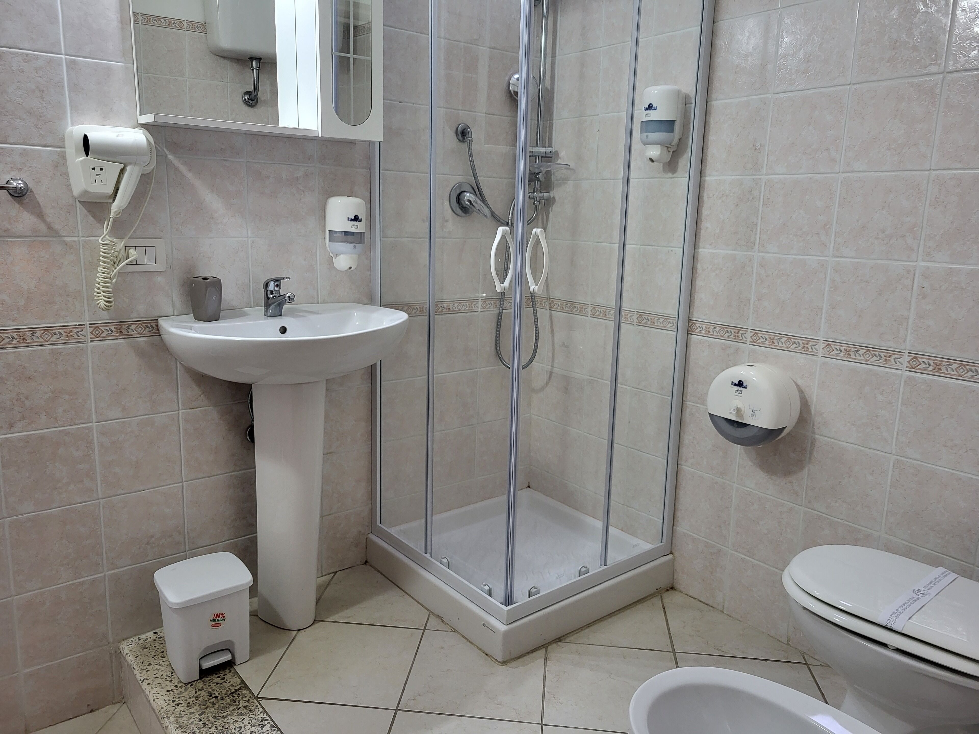 A bathroom with a glass-enclosed shower, a sink, a toilet, and a trash bin.