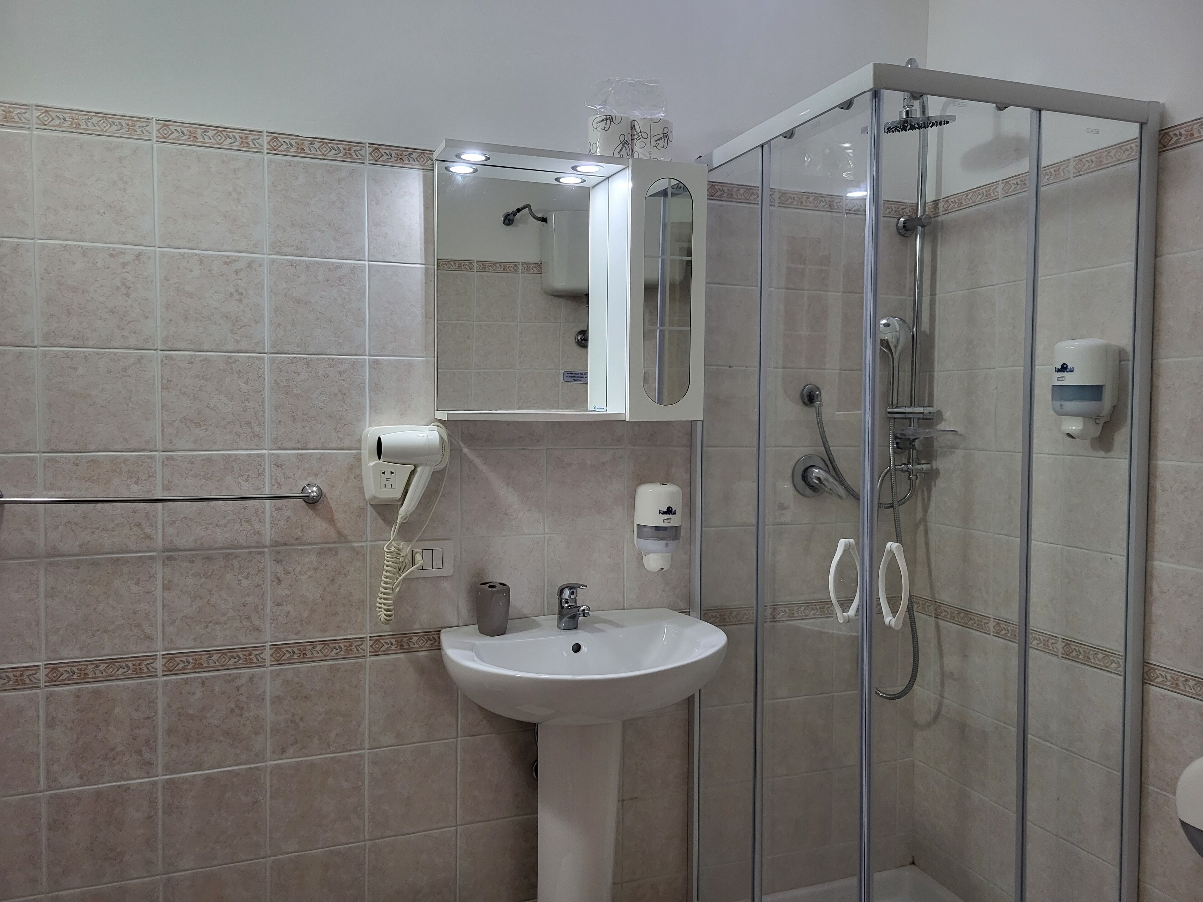 A bathroom with a glass-enclosed shower, a white sink, and a hairdryer mounted on the wall.