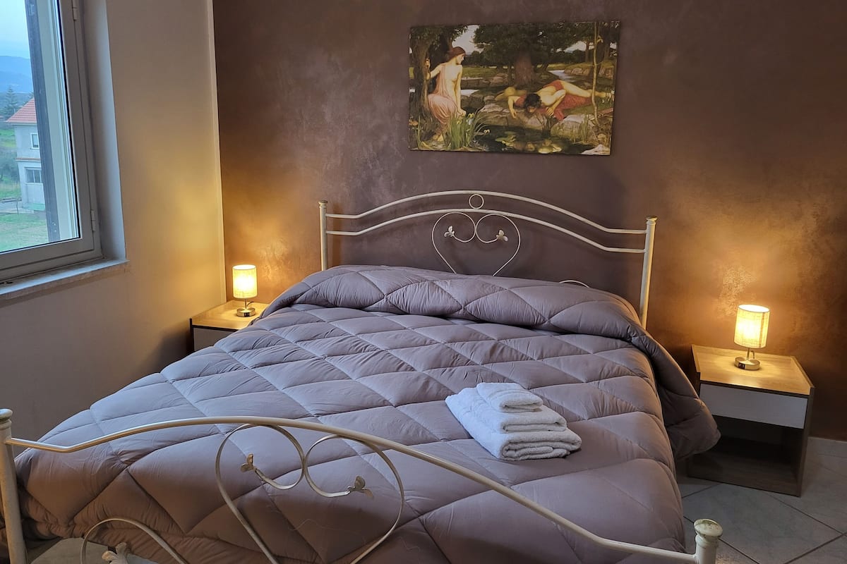 Ein Schlafzimmer mit einem Bett, zwei Nachttischen, einem Fenster und einem Bild an der Wand.