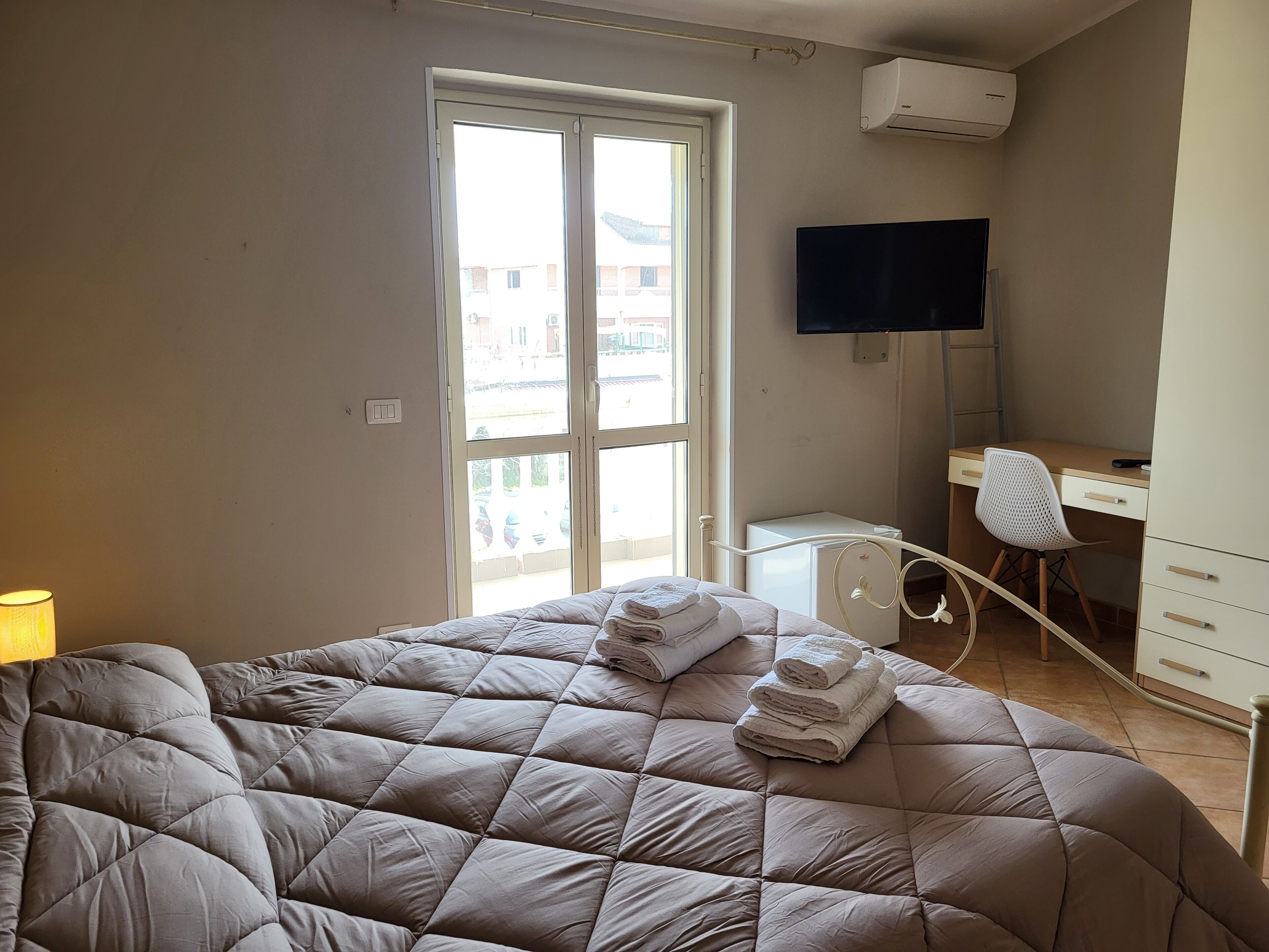 A bedroom with a bed, a desk, a chair, and a TV.