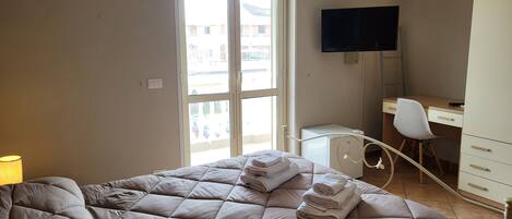 A bedroom with a bed, a desk, a chair, and a TV.