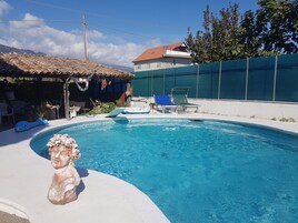 Piscina con una estatua, un porche cubierto y un área vallada con sillas de descanso.