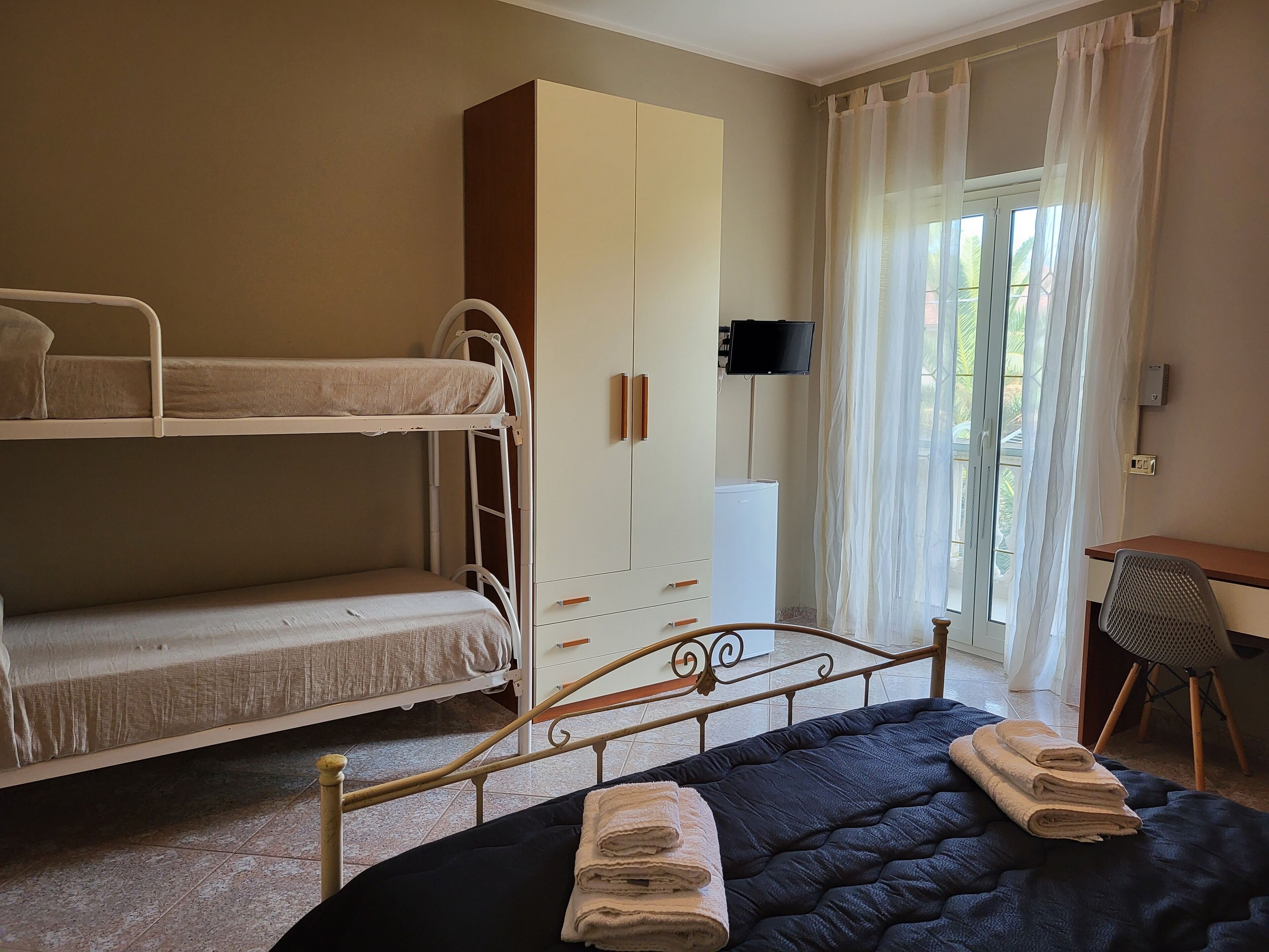 A room with bunk beds, a wardrobe, a desk, a chair, and a television.