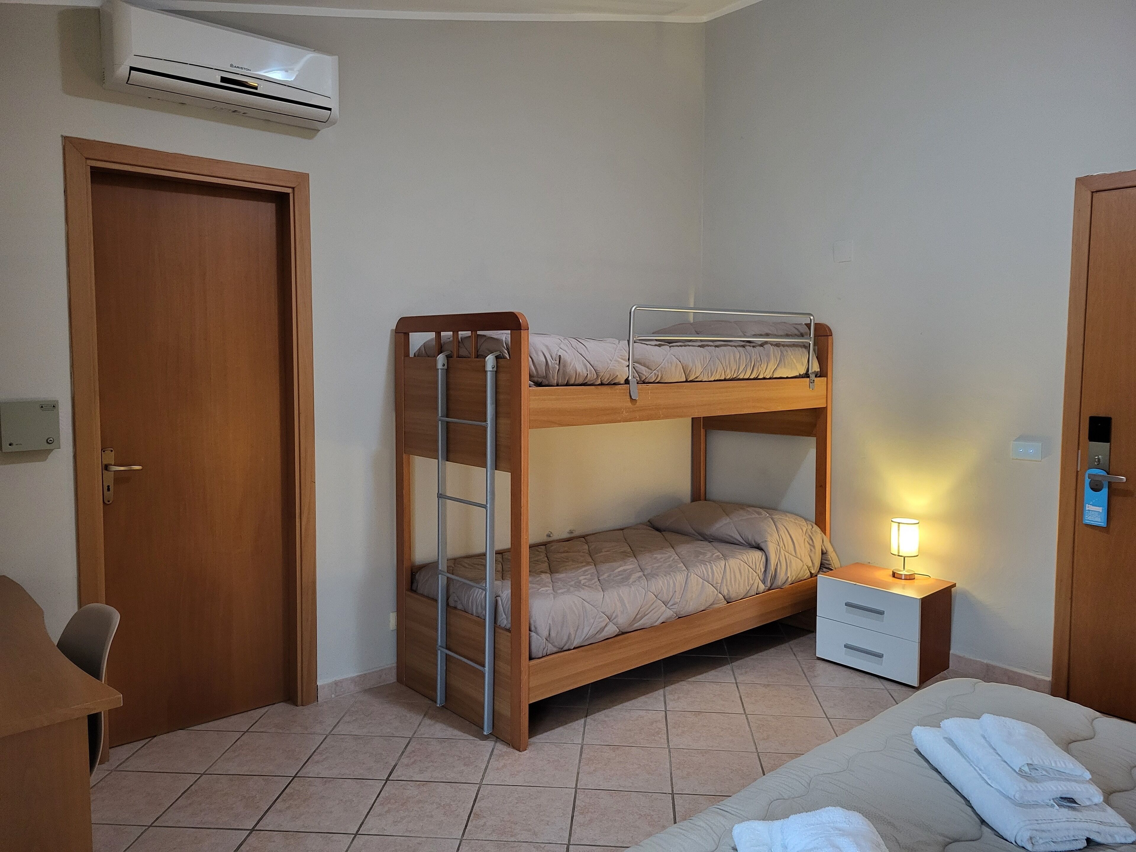 A bunk bed with a ladder, a bedside table with a lamp, and a door with a lock.