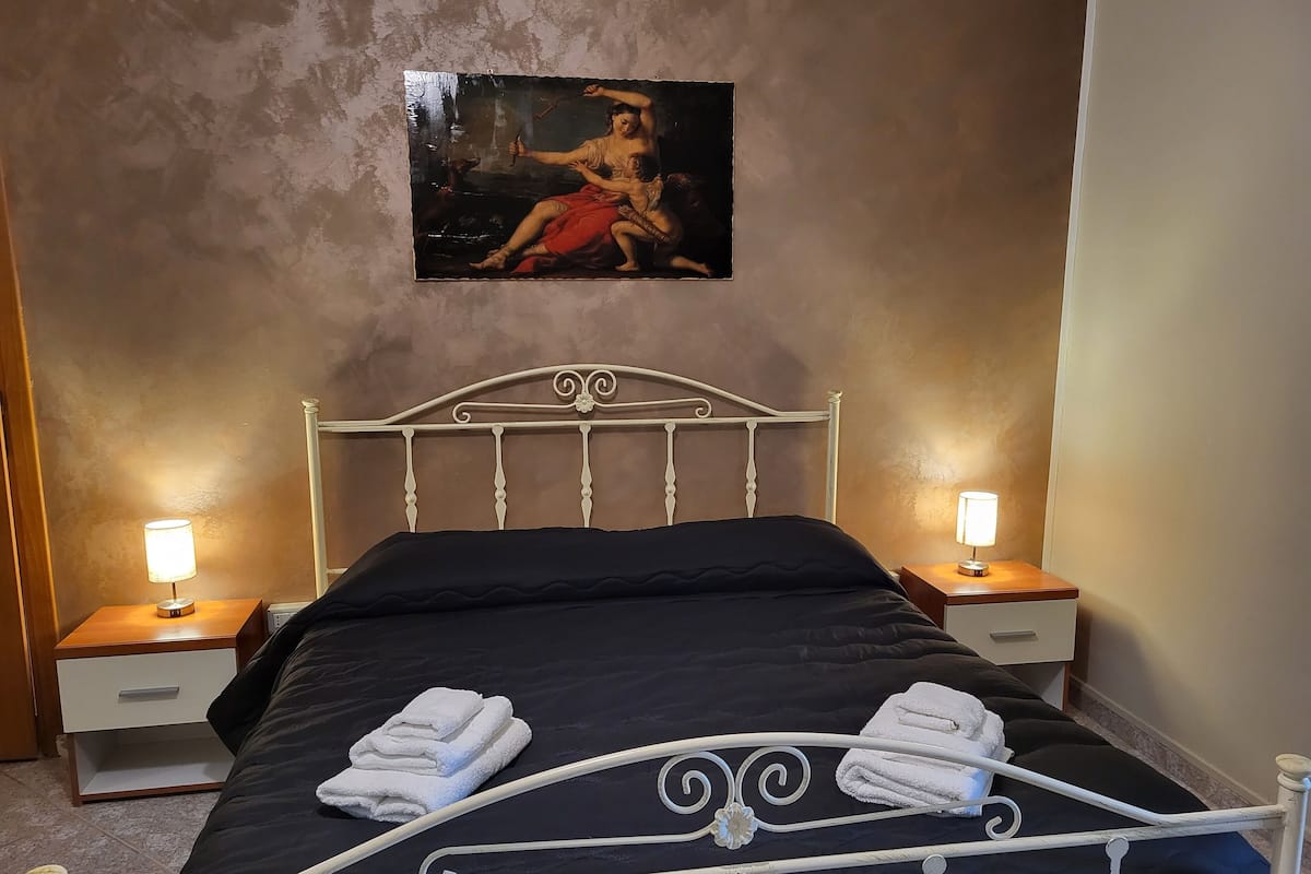 Ein Schlafzimmer mit einem Bett, zwei Nachttischen, einem Bild an der Wand und zwei Lampen.