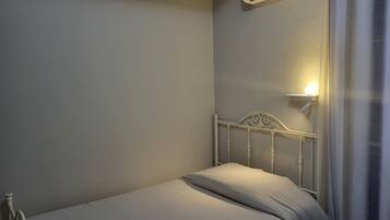 A single bed with a white headboard, a bedside table with a lamp, and an air conditioning unit mounted on the wall.