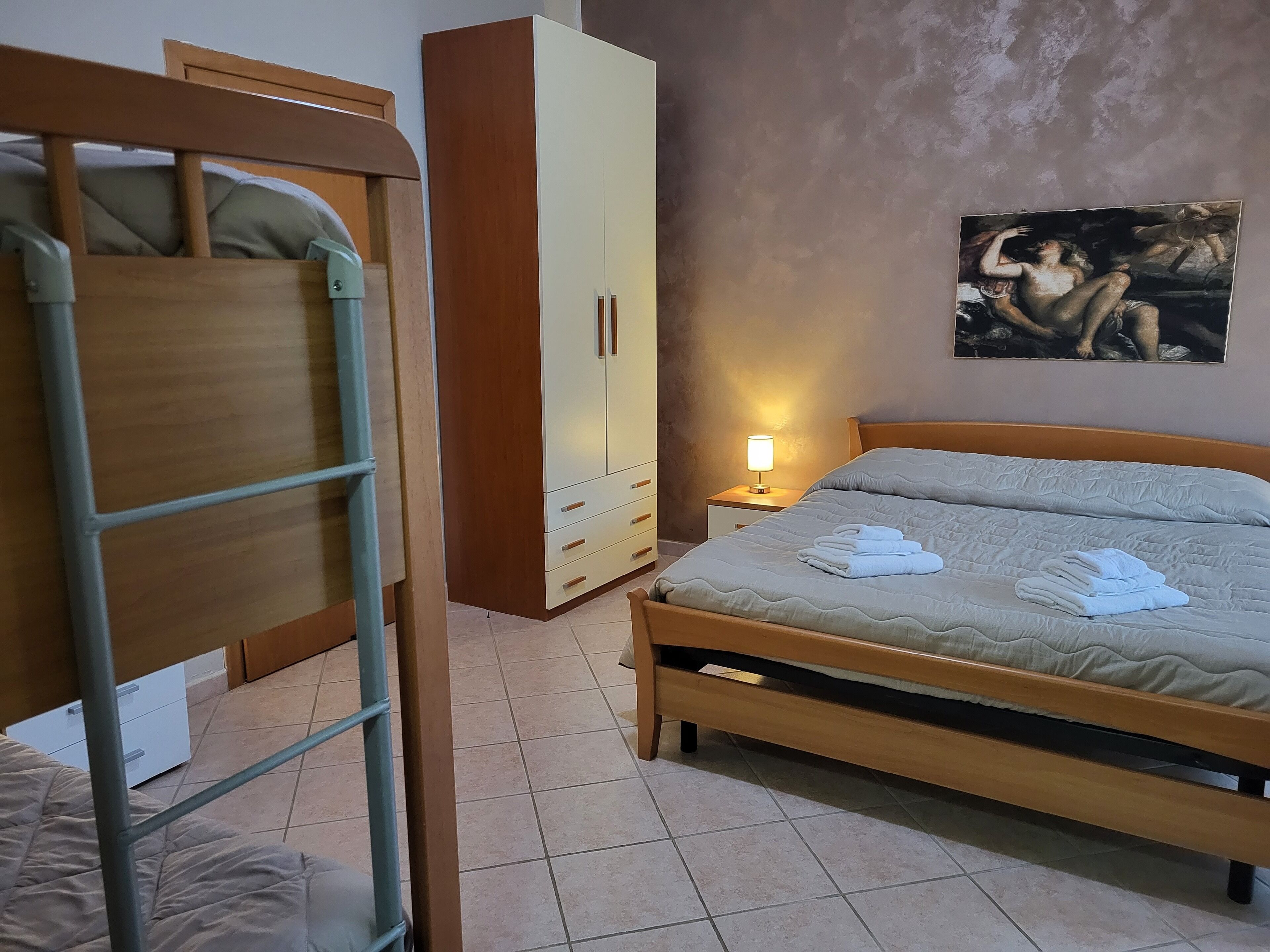 Un dormitorio con literas, un armario, una mesita de noche con lámpara y un cuadro en la pared.