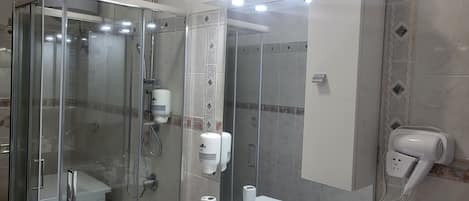 Un baño moderno con ducha de vidrio, lavamanos blanco con espejo y secador de pelo en la pared.