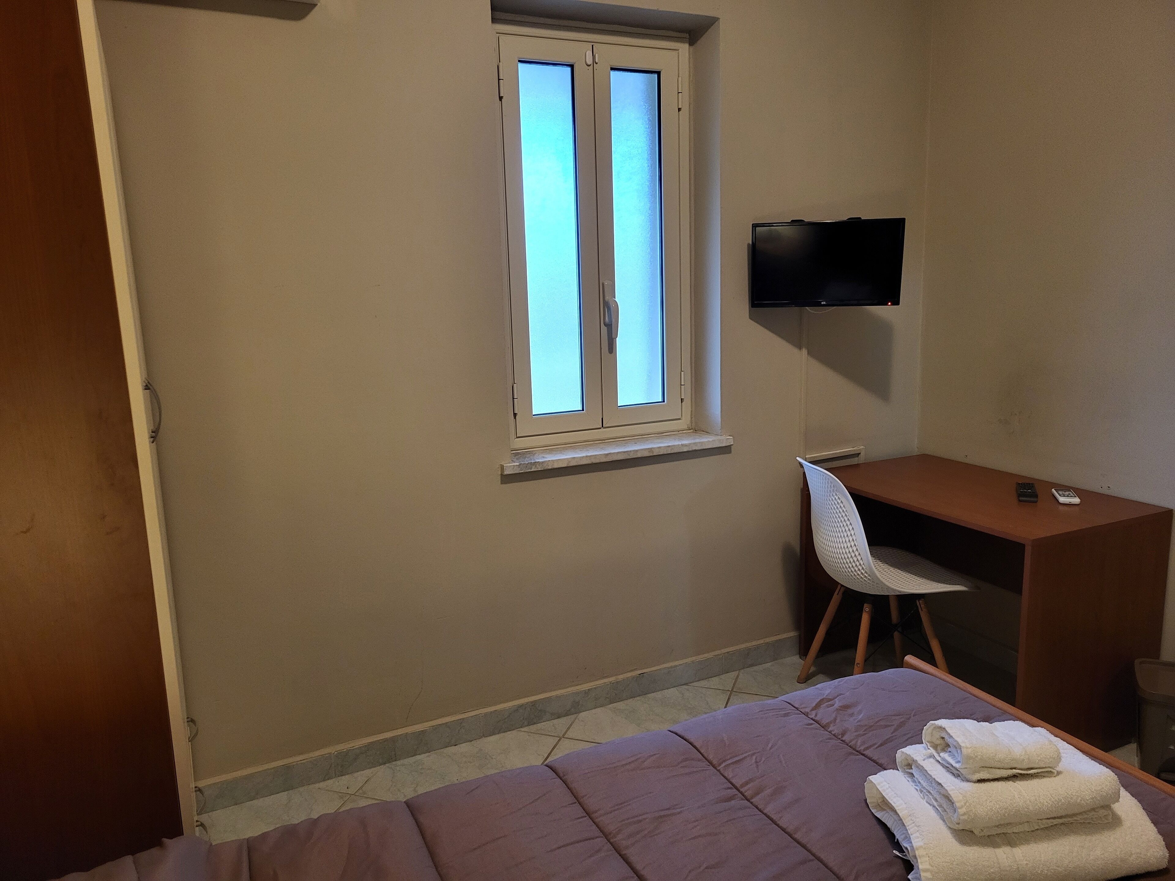 Un dormitorio con cama, escritorio, silla, televisor y ventana.
