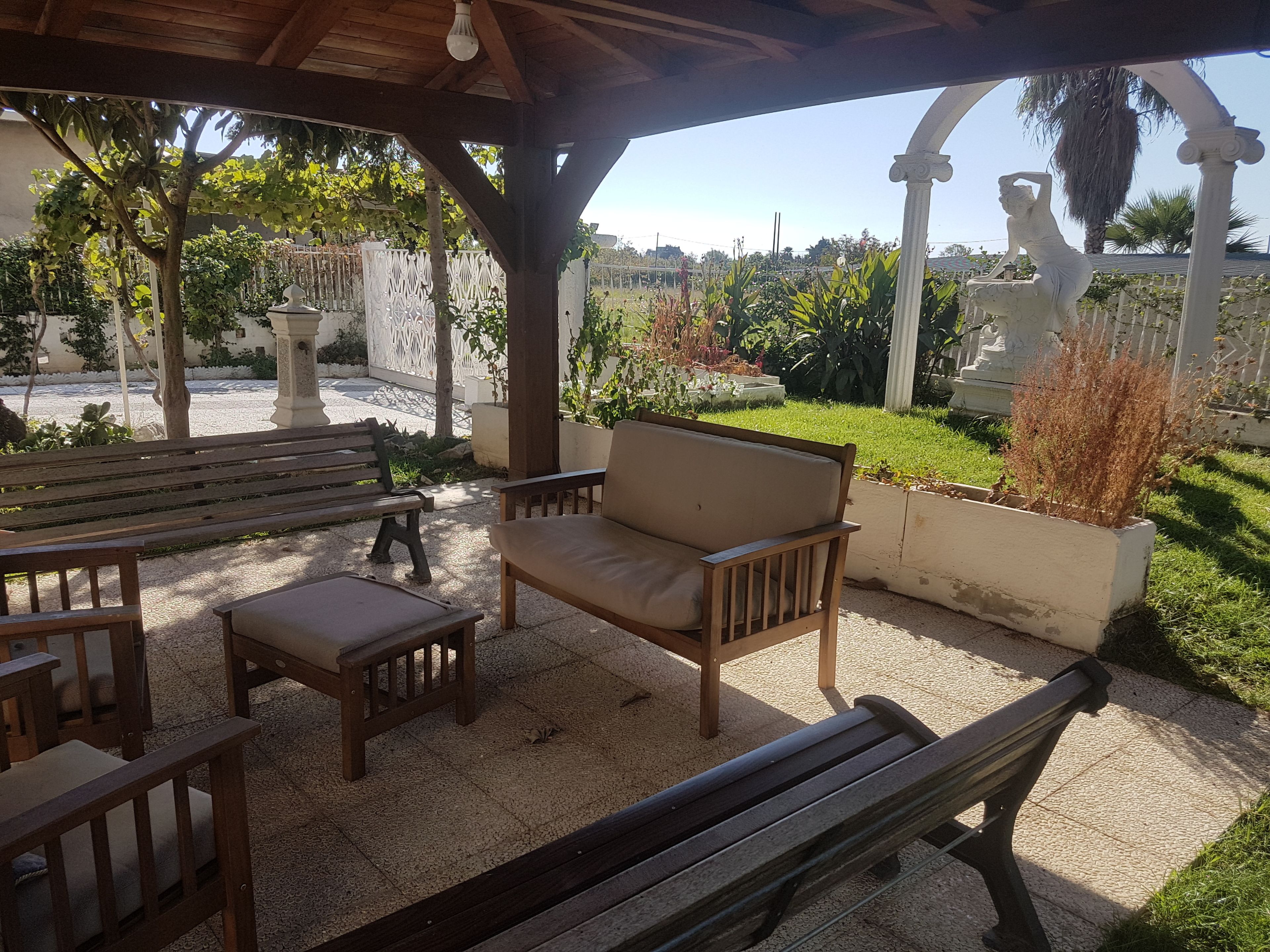 A covered outdoor seating area with wooden benches and a cushioned sofa.