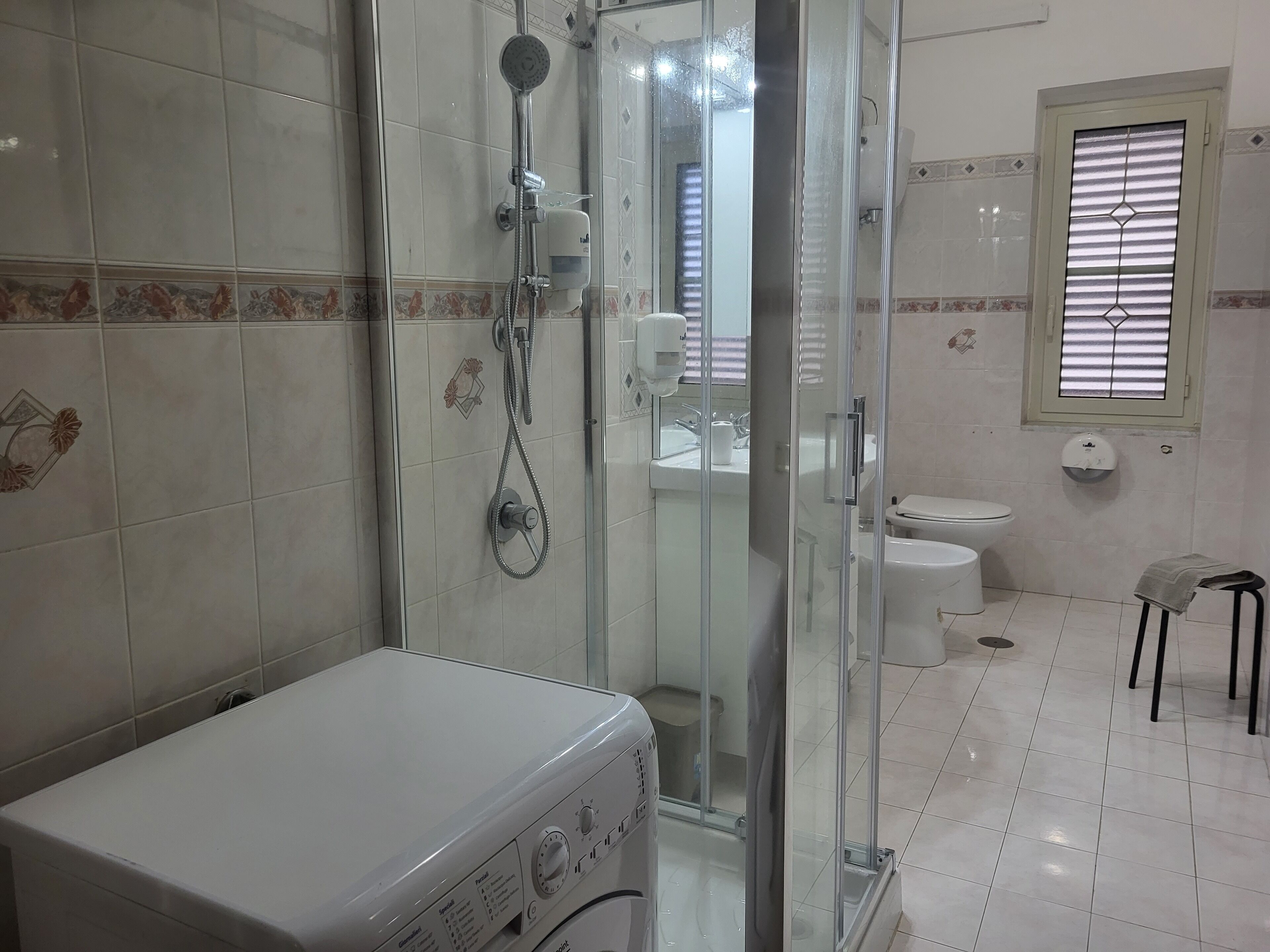 A bathroom with a glass-enclosed shower, a toilet, and a washing machine.