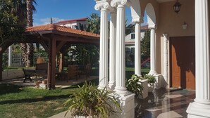 Área externa coberta com pérgola, assentos e plantas em vasos.