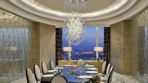 Un comedor lujoso con una gran lámpara de araña, vistas de la ciudad a través de las ventanas y una mesa con una decoración moderna.