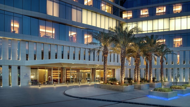 Un hotel moderno con fachada de vidrio, palmeras y una entrada bien iluminada.