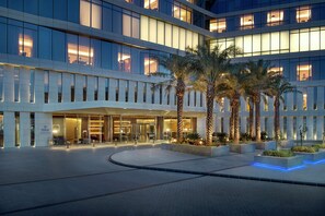 Un hotel modern amb façana de vidre, palmeres i una entrada ben il·luminada.
