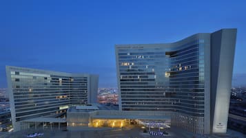 A modern hotel with a curved facade and multiple floors, featuring a prominent entrance with a covered area and a view of the cityscape in the background.