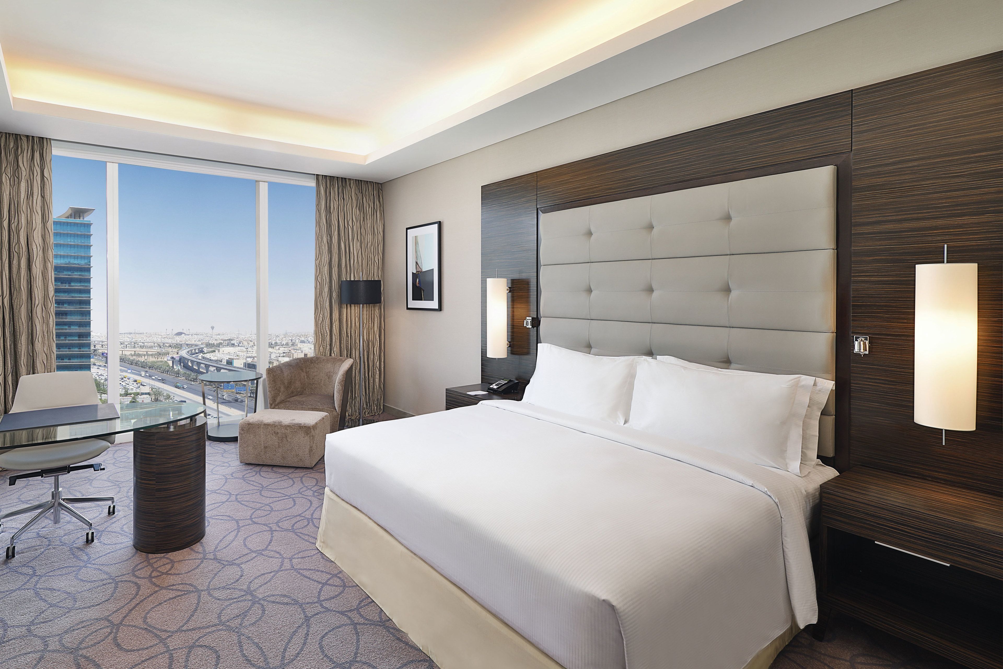 Een hotelkamer met een groot bed, een glazen tafel, een stoel en uitzicht op een stadsbeeld.