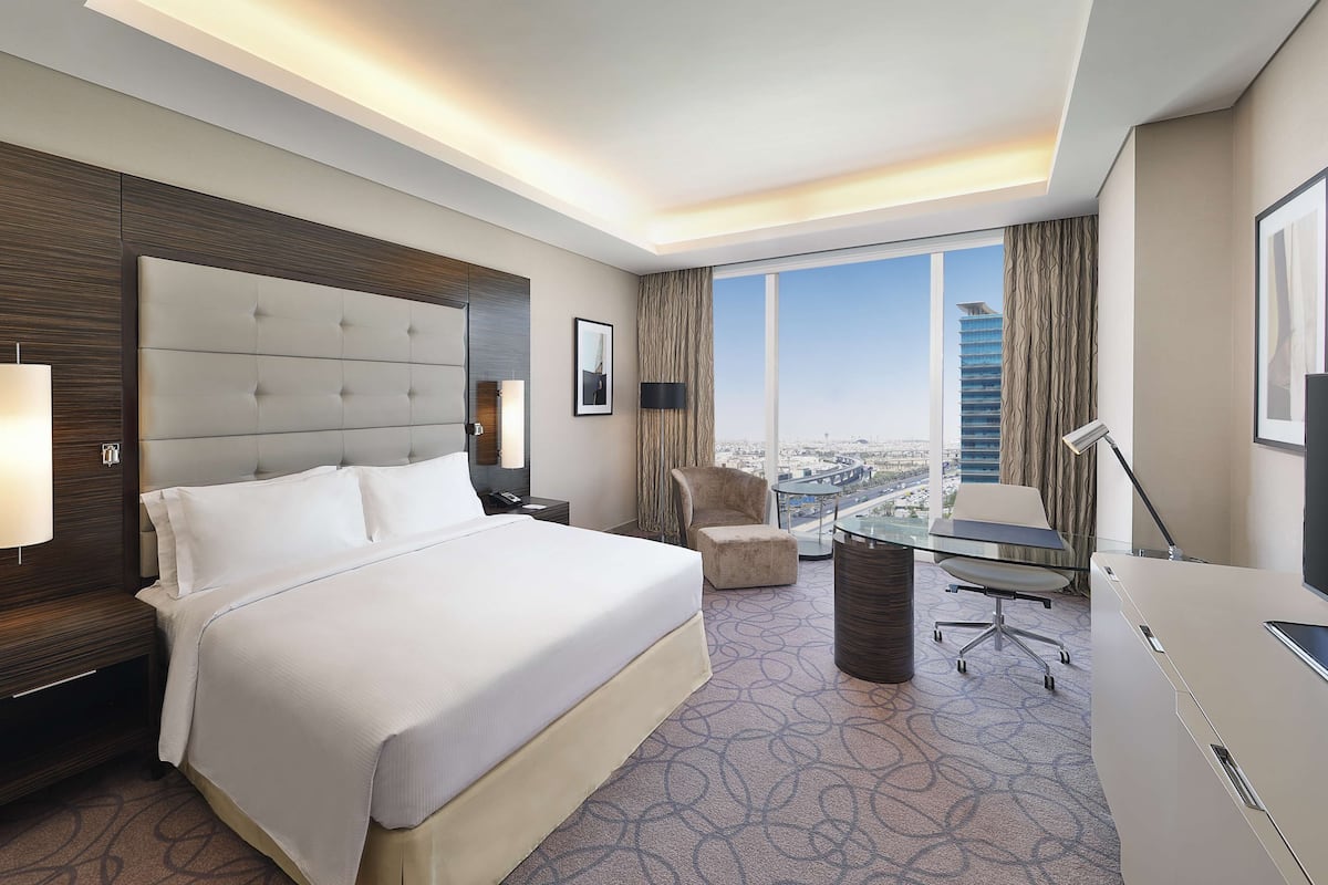 Habitación de hotel con una cama grande, un escritorio, una silla, un televisor y vistas a un paisaje urbano.