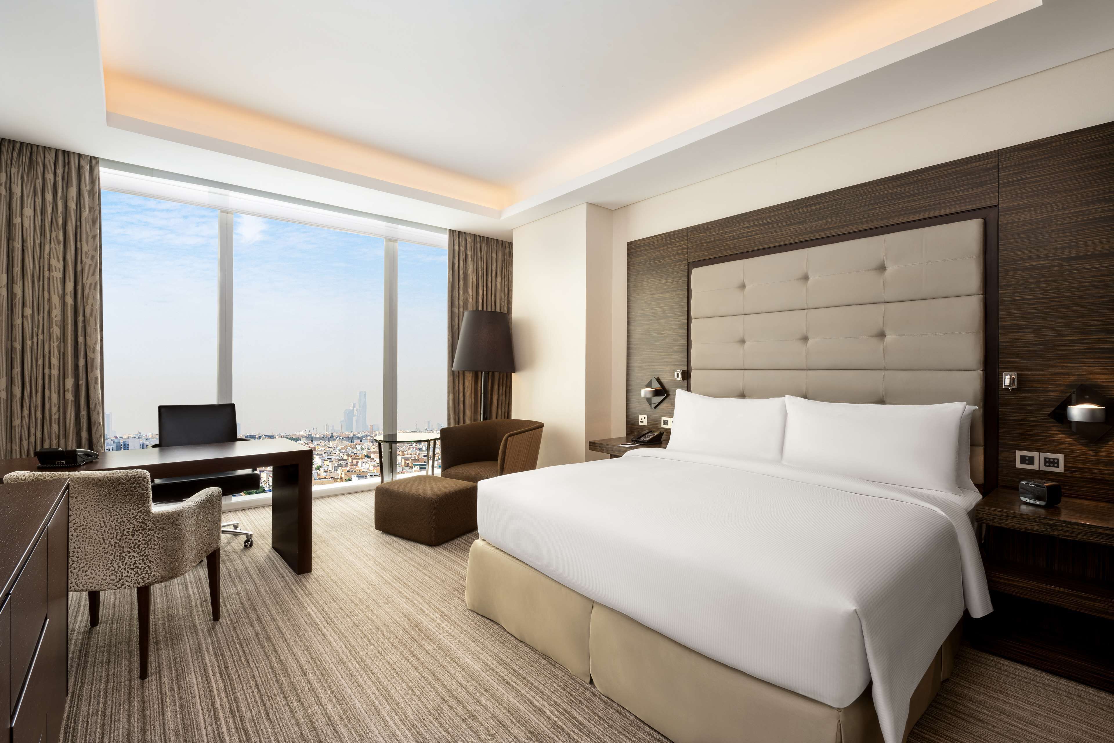 Une chambre d’hôtel avec un grand lit, un bureau, une chaise, une lampe et une vue sur la ville.