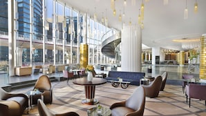 Un moderno vestíbulo de hotel con una escalera curva, zonas de descanso y amplios ventanales con vistas a la ciudad.