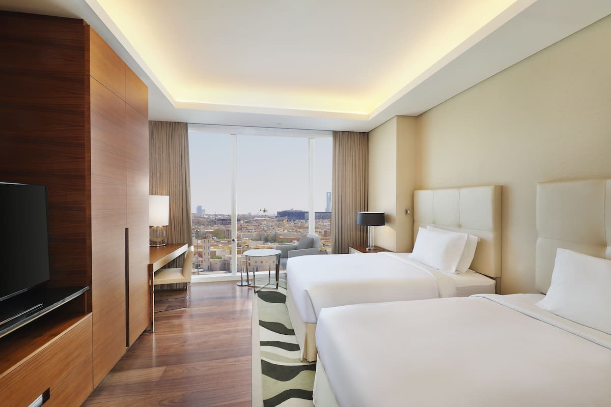 Habitación de hotel con dos camas, televisión, escritorio y vistas a la ciudad.