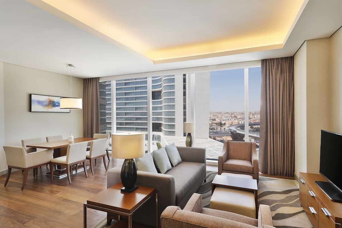 Una habitación de hotel moderna con un ventanal grande, un sofá, una mesa de comedor y un televisor.