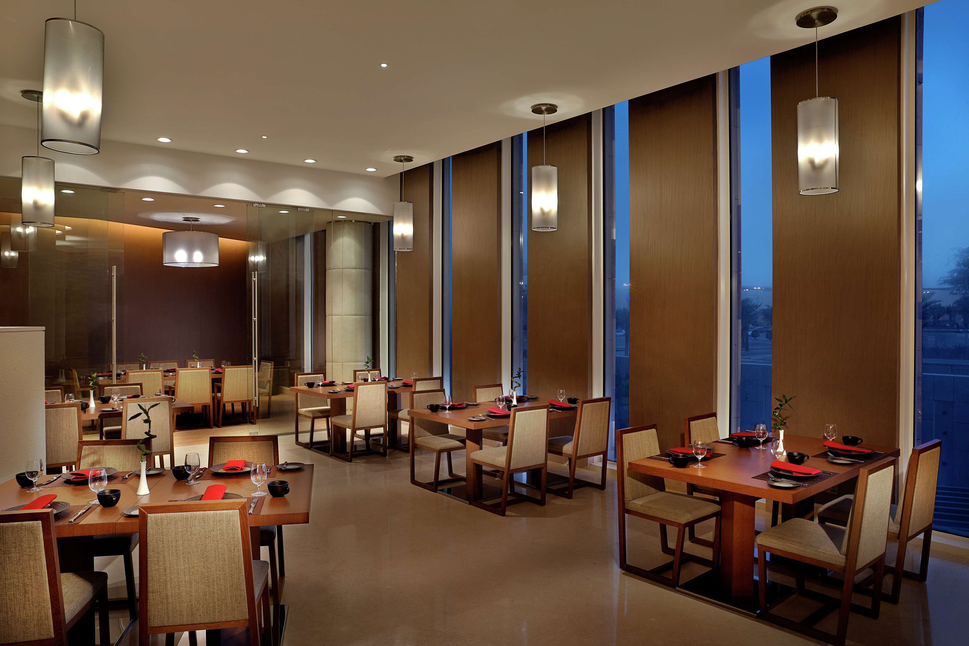 Un espace de restauration moderne doté de plusieurs tables et chaises, de grandes fenêtres et d’un éclairage contemporain.