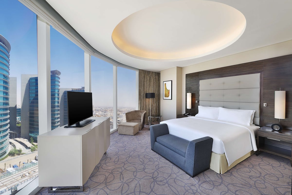 Una habitación de hotel moderna con una cama grande, un televisor en un mueble, un escritorio y vistas a la ciudad.