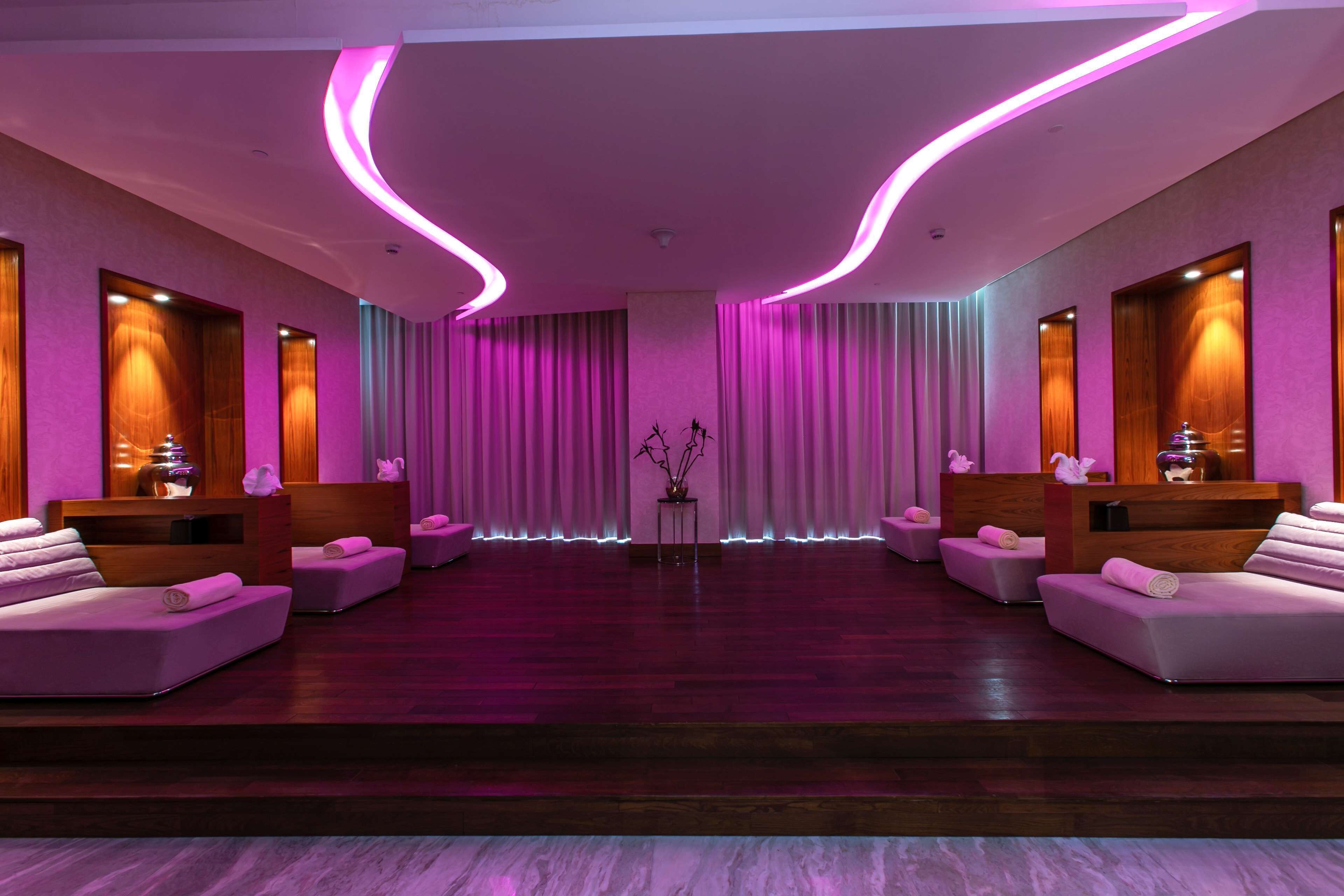Ein moderner Wellnessraum mit Holzboden, zwei weißen Sofas, einem kleinen Tisch mit einer Vase und rosafarbenen Vorhängen.
