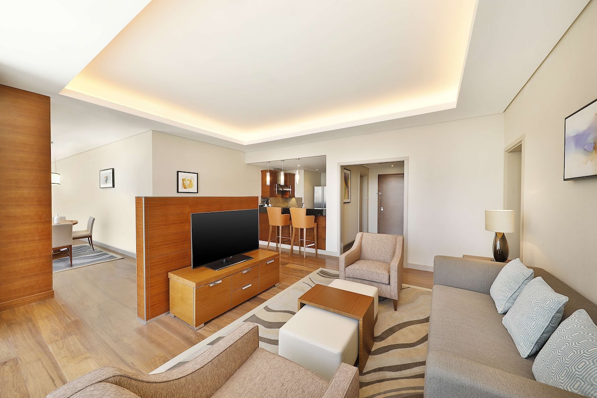 Una sala de estar moderna con un televisor de pantalla plana, muebles de madera, un sofá y un comedor con sillas.