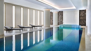 Una amplia piscina interior con agua cristalina y azul, rodeada de tumbonas y un diseño interior moderno.