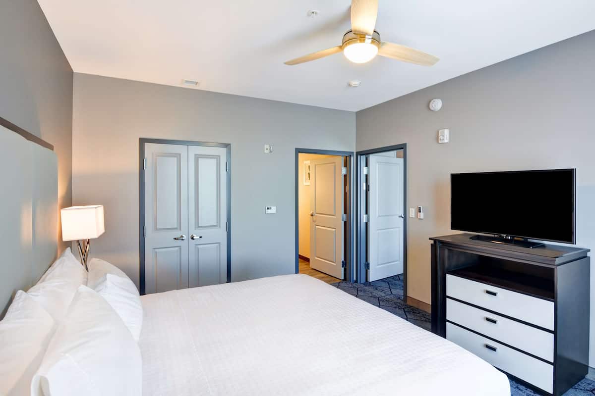 A hotel room with a bed, a television on a stand, and two doors leading to other rooms.