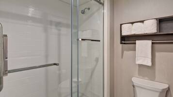 Een badkamer met een douchecabine van glas, een toilet en een plank met handdoeken.