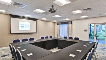 A conference room with a long table, chairs, a projector screen displaying "Homewood Suites by Hilton," and a door leading outside.
