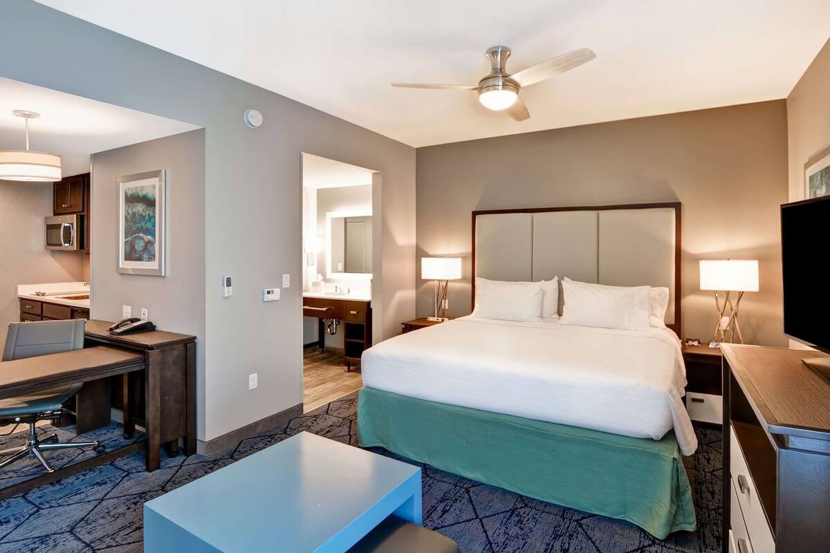 A hotel room with a bed, desk, chair, and a ceiling fan.